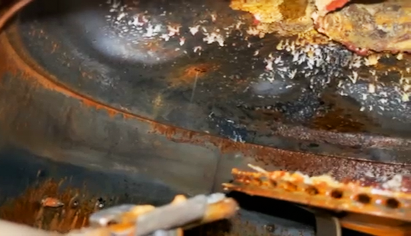 Severely corroded interior of a water heater tank showing rust, scale, and metal damage.